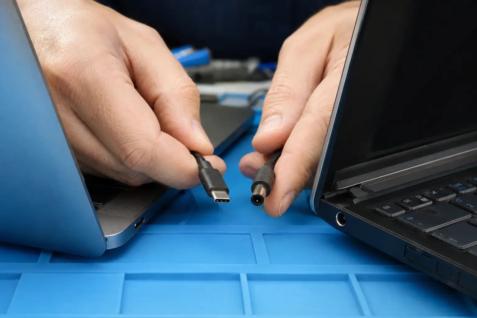 USB-C and round barrel laptop charger connectors being checked beside matching charging ports