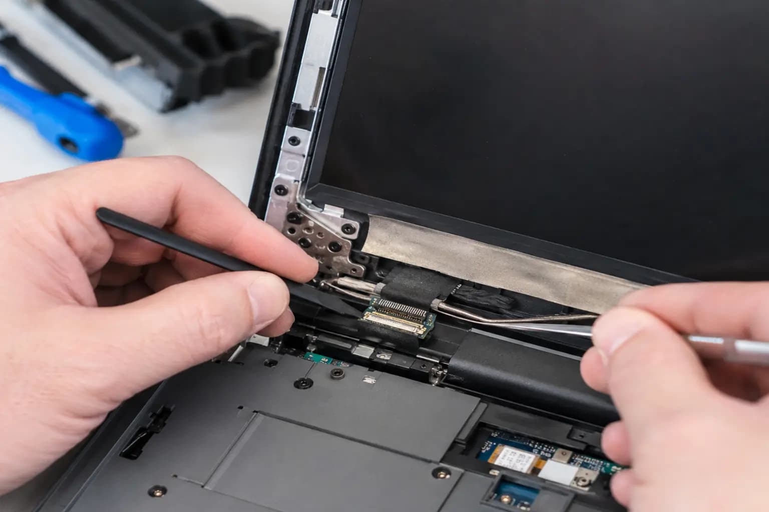 Technician inspecting a laptop display cable and hinge area with precision tools