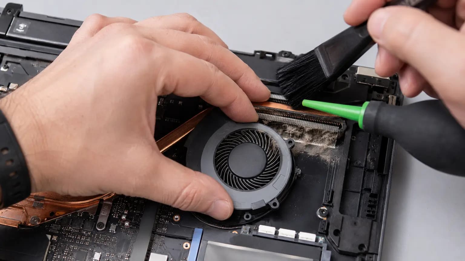 Technician safely cleaning dust from a laptop cooling fan and heatsink fins