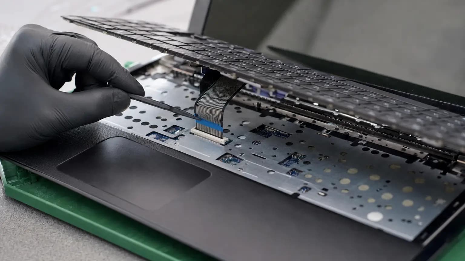 Technician inspecting a laptop keyboard ribbon cable and locking connector