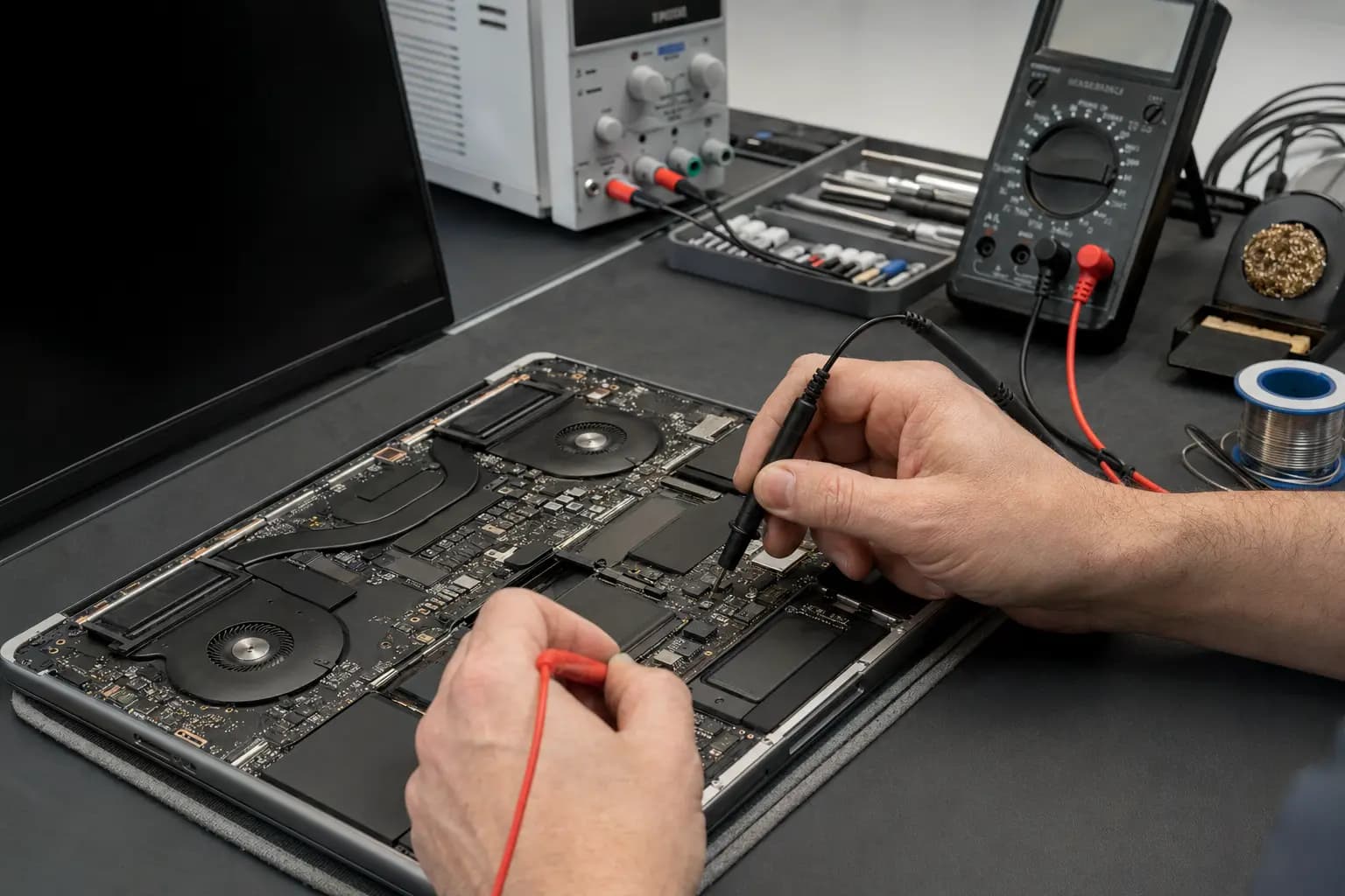 Technician measuring laptop motherboard power rails with a bench supply and multimeter