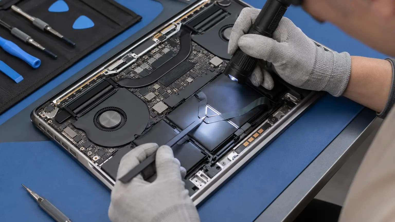 Technician inspecting a laptop touchpad ribbon cable and battery area