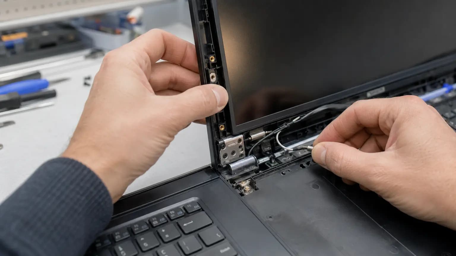 Technician checking display cable and Wi-Fi antenna wiring beside a damaged laptop hinge