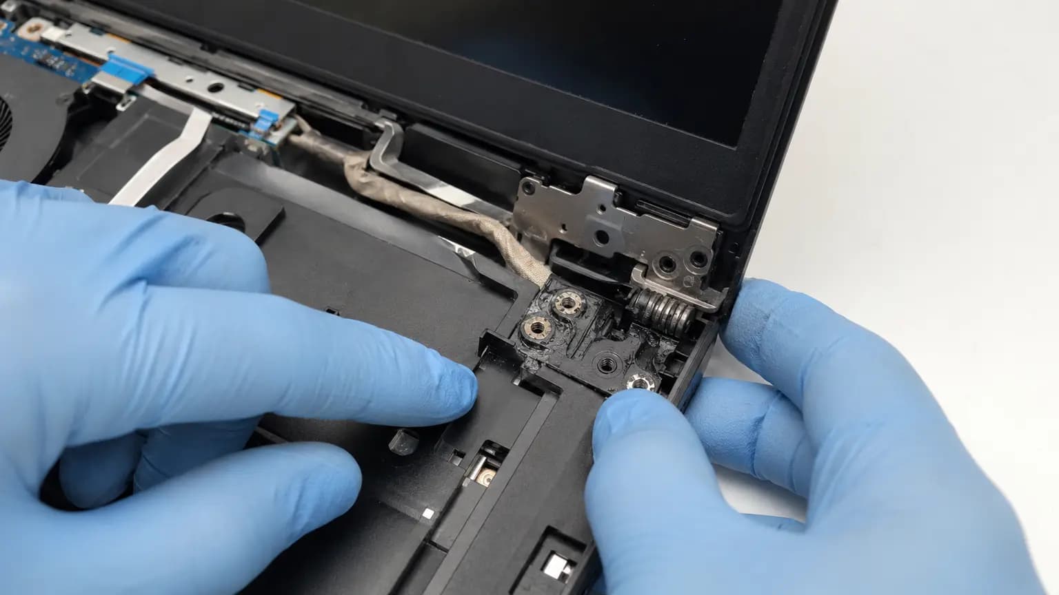 Technician inspecting a laptop hinge bracket and cracked internal mounting points